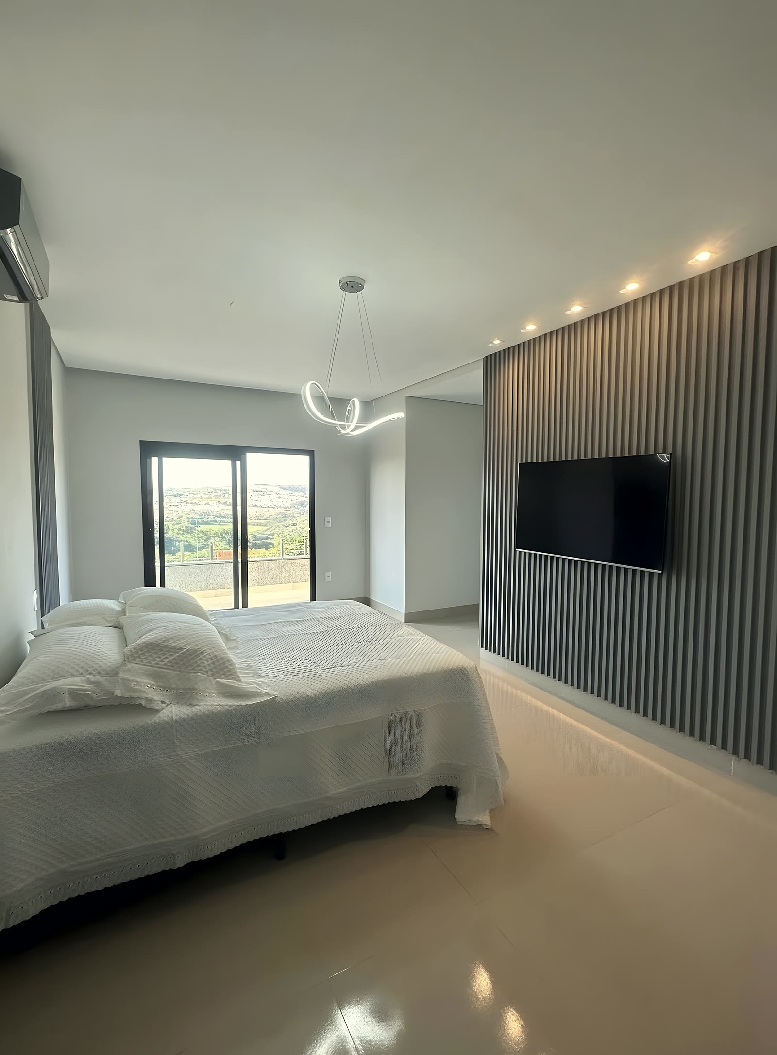 Suíte com cama de casal, painel ripado e vista para a serra